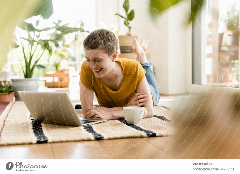 Smiling mid adult woman using laptop while lying on carpet at home color image colour image Germany leisure activity leisure activities free time leisure time