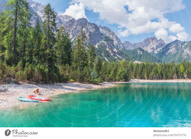 Man by paddleboards at Pragser Wildsee lakeshore on sunny day, Dolomites, Alto Adige, Italy color image colour image outdoors location shots outdoor shot