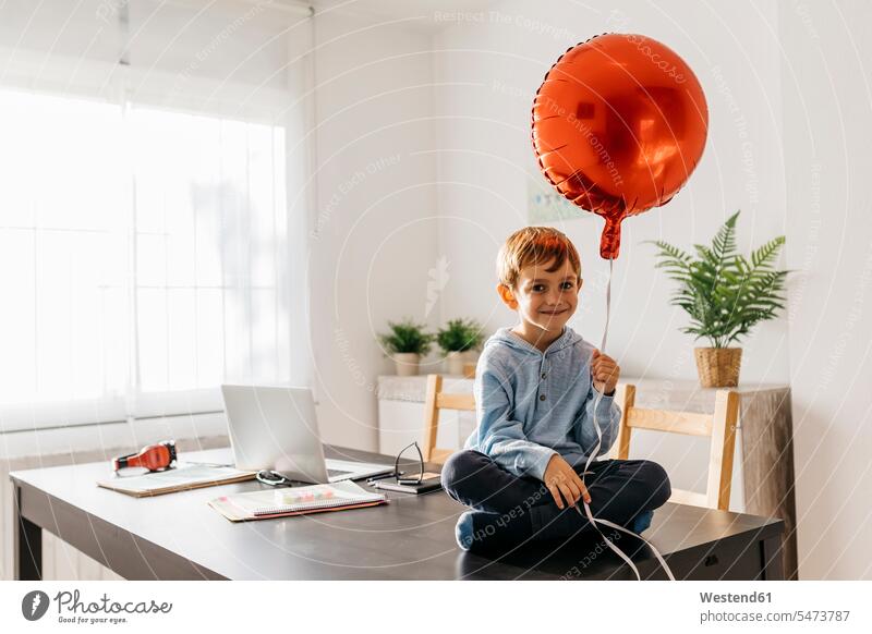 Boy sitting on the dining table with a red balloon in his hand Seated balloons full length full-length full-body full body full shot optimistic optimism