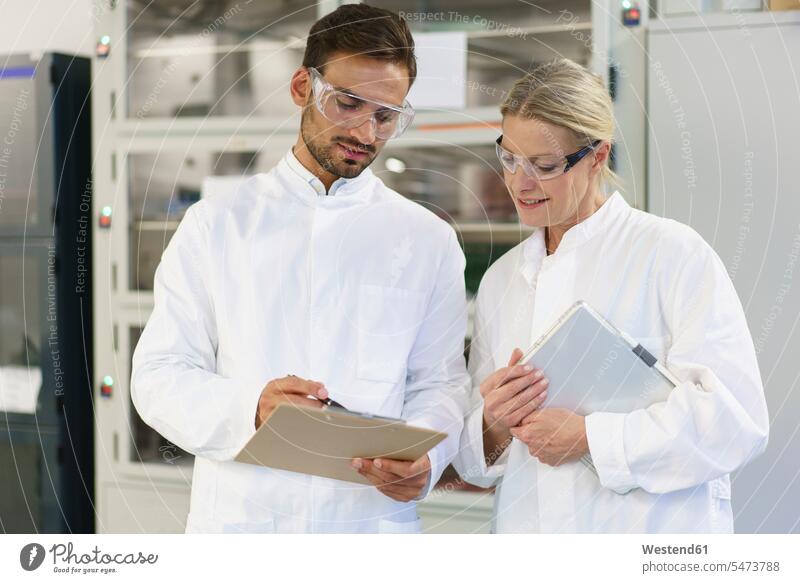 Young male technician discussing over clipboard with female blond colleague holding digital tablet at laboratory color image colour image indoors indoor shot