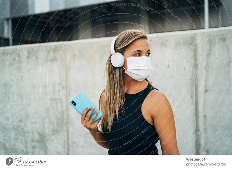 Young athletic woman with protective mask, headphones and smartphone headset telecommunication telephone telephones cell phone cell phones Cellphone mobile