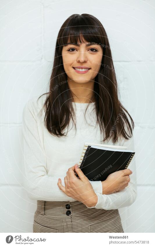 Portrait of smiling young woman with notebook at brick wall females women brick walls smile portrait portraits standing notebooks Adults grown-ups grownups