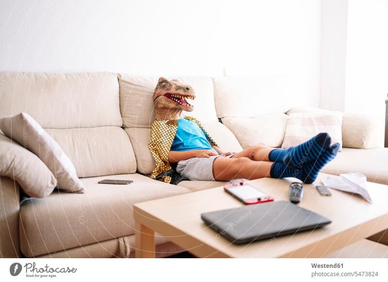 Boy wearing dinosaur mask relaxing on sofa at home color image colour image Spain indoors indoor shot indoor shots interior interior view Interiors
