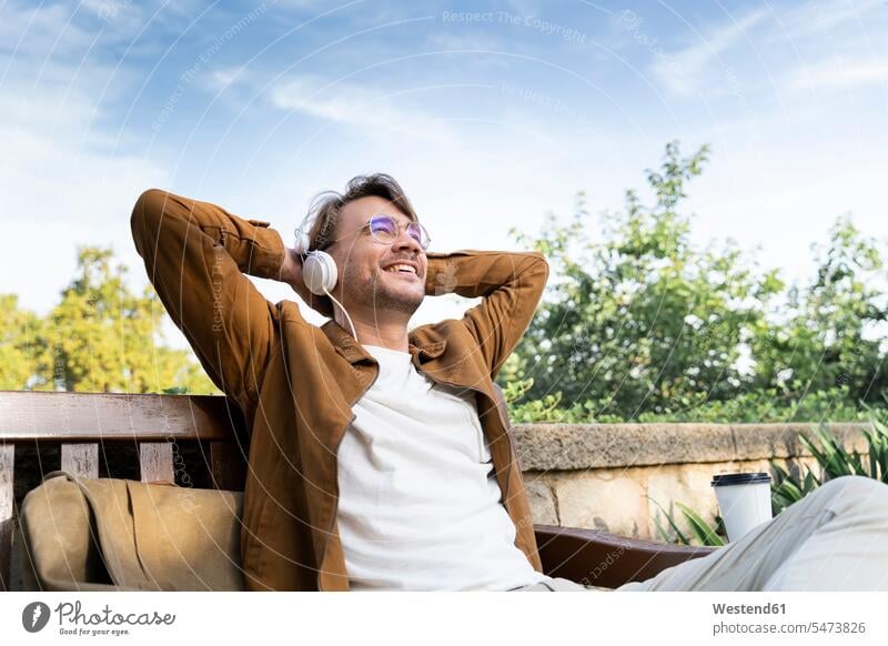 Laughing man sitting on bench listening music with headphones human human being human beings humans person persons caucasian appearance caucasian ethnicity
