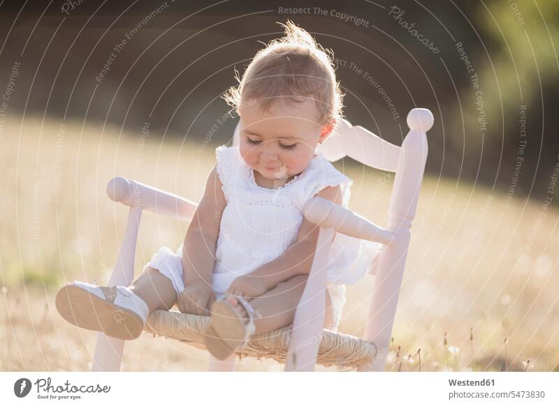 Cute baby girl sitting on chair on meadow during sunny day color image colour image Spain outdoors location shots outdoor shot outdoor shots daylight shot