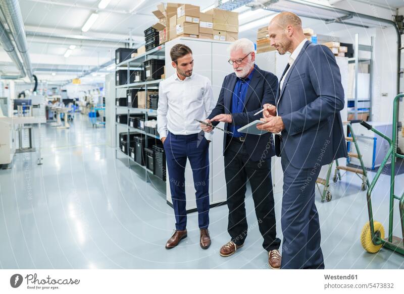 Senior manager discussing over machine part with male colleagues while standing at illuminated factory color image colour image indoors indoor shot indoor shots