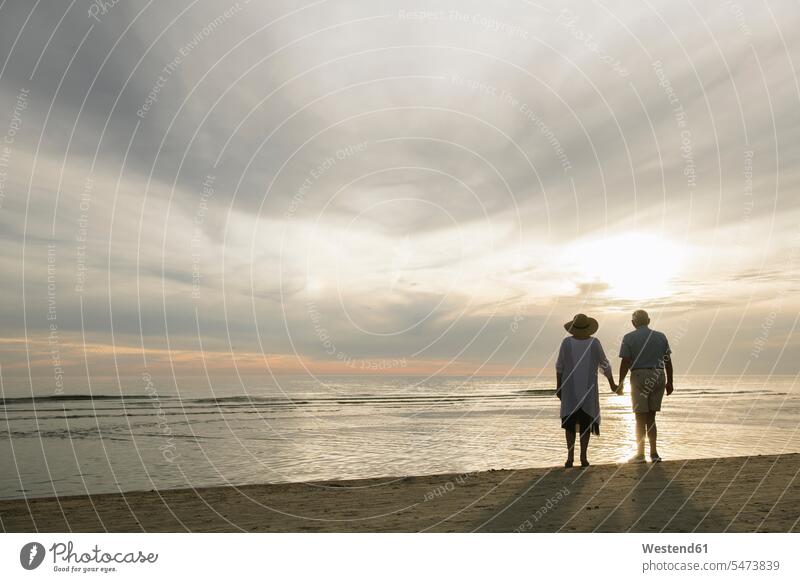 Back view of senior couple standing hand in hand on the beach watching sunset, Liepaja, Latvia human human being human beings humans person persons