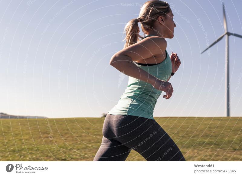 Young woman jogging on field way, wind wheels in the background windmills wind turbine wind turbines dirt track field path field paths eco-friendly sustainable