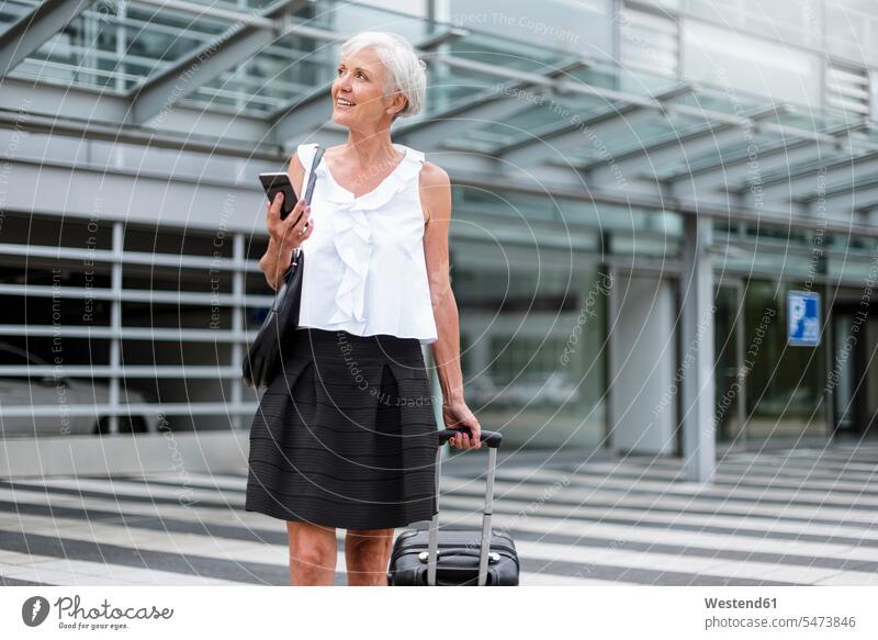 Smiling senior woman with cell phone and baggage on the move senior women elder women elder woman old females luggage mobile phone mobiles mobile phones