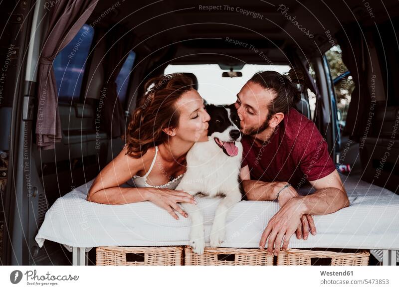 Smiling couple kissing dog while lying in camper trailer color image colour image Spain leisure activity leisure activities free time leisure time dogs Canine