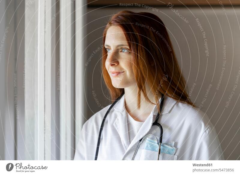 Smiling young female doctor looking through window color image colour image Female Doctor Female Doctors doctors physician physicians healthcare and medicine