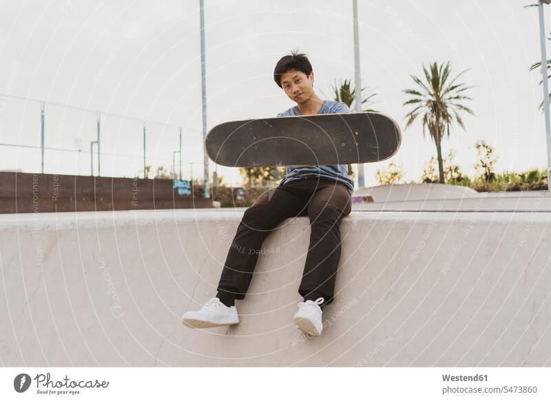 Young Chinese man sitting on wall of a skate park near the beach Chinese Ethnicity young beaches skateboarder skater skateboarders skaters Seated walls