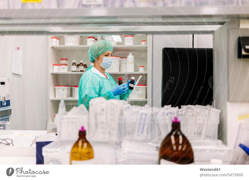 Female pharmacist holding bottles while standing by shelf in hospital color image colour image Spain indoors indoor shot indoor shots interior interior view