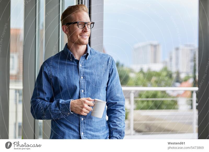 Smiling young man with cup of coffee standing at balcony door Coffee Cup Coffee Cups balcony doors men males Drink beverages Drinks Beverage food and drink
