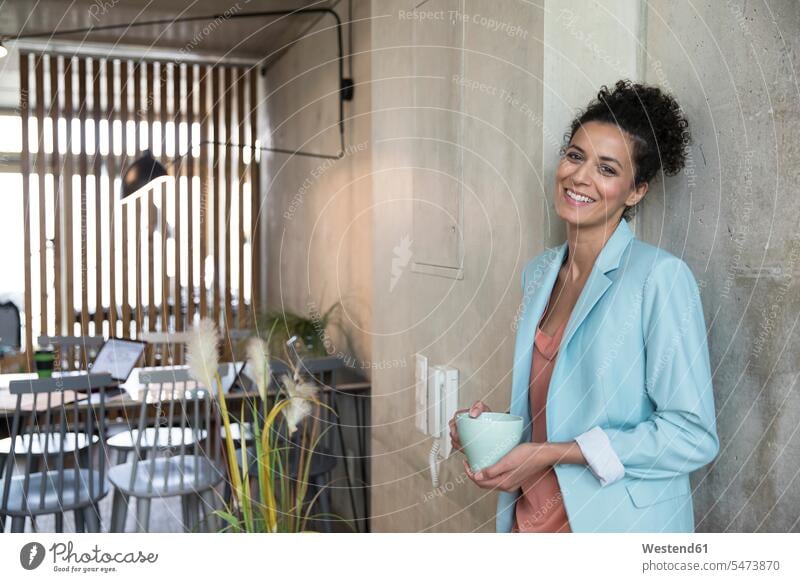 Portrait of smiling businesswoman holding coffee mug at concrete wall in a loft concrete walls portrait portraits lofts businesswomen business woman