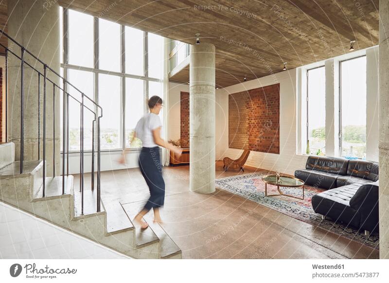 Woman walking down stairs in a loft flat windows couches settee settees sofa sofas go going clear fair light interior equipment free time leisure time Distinct