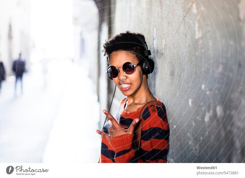 Portrait of young woman listening music with headphones showing Rock And Roll Sign hearing females women Sign of the Horns Horn Signs portrait portraits Adults