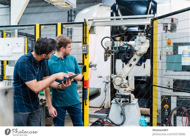 Male coworkers holding digital tablet looking at robotic arm while standing in manufacturing industry color image colour image indoors indoor shot indoor shots