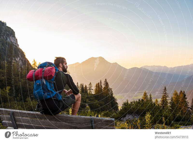 Austria, Tyrol, Hiker taking a break, sitting on bench, looking at view wooden bench Taking a Break resting sunset sunsets sundown Seated beauty of nature