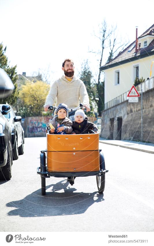 Happy father with two children riding cargo bike in the city pa fathers daddy dads papa cargo bicycle town cities towns babies infants baby happiness happy