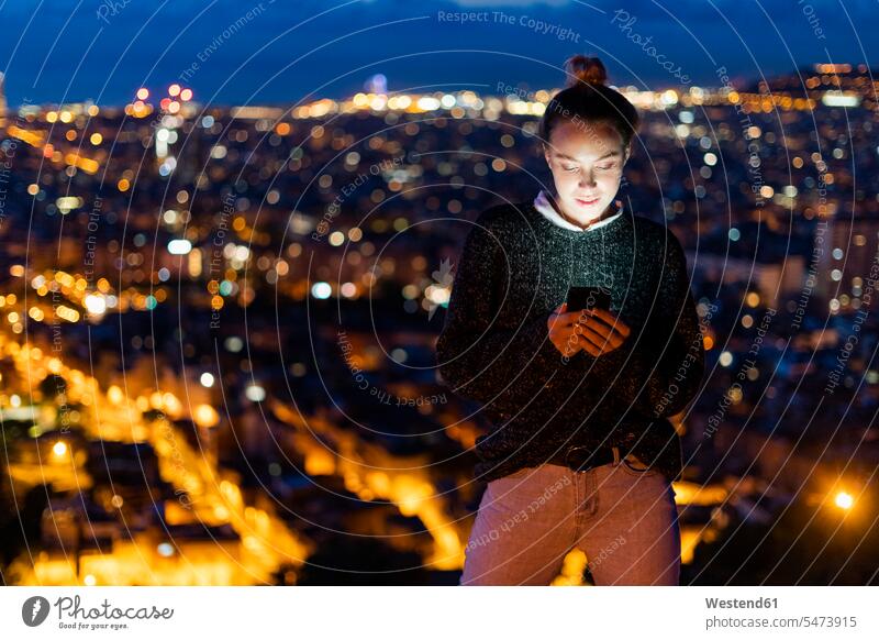 Young woman using cell phone at night above the city, Barcelona, Spain human human being human beings humans person persons caucasian appearance