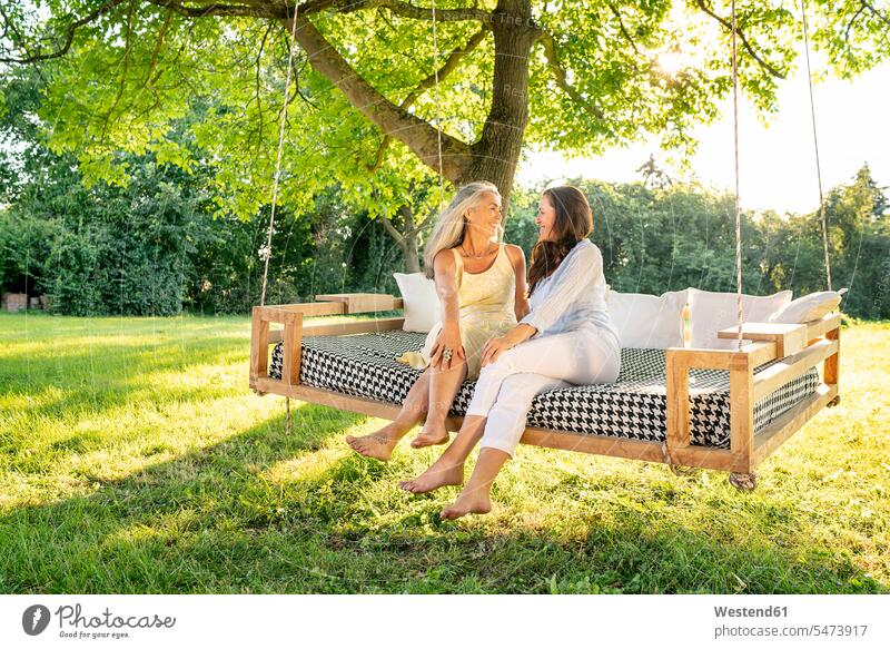 Two women relaxing on a hanging bed in garden female friends hammock hammocks woman females relaxed relaxation gardens domestic garden beds mate friendship