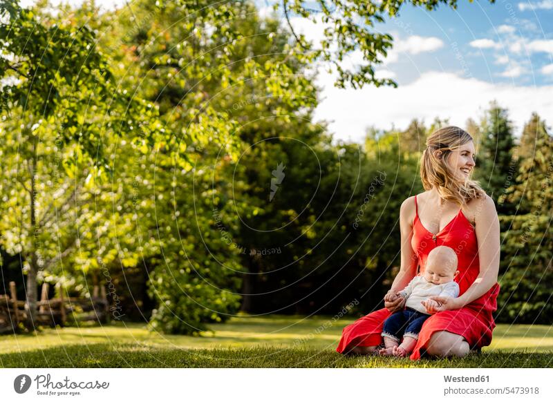 Smiling mother holding baby boy while kneeling on grassy land in park color image colour image Canada leisure activity leisure activities free time leisure time