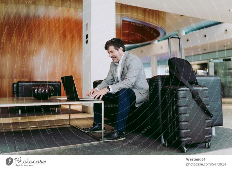 Mature businessman using laptop while sitting in hotel lobby color image colour image indoors indoor shot indoor shots interior interior view Interiors day