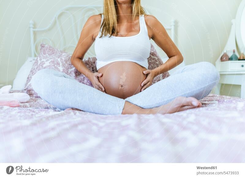 Close-up of belly of pregnant woman sitting on the bed beds bellies stomach stomachs females women Pregnant Woman Seated upper body upper part of the body