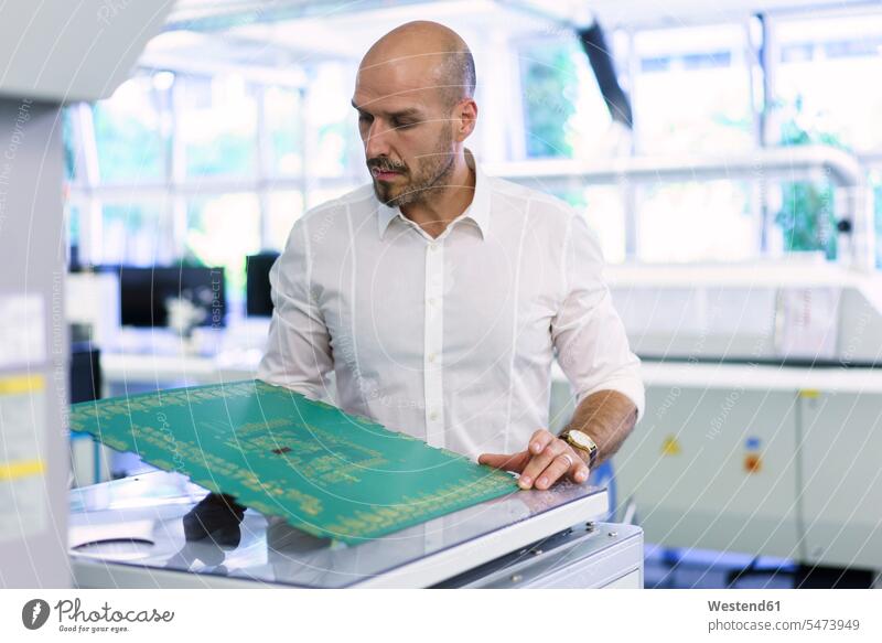 Confident mature male technician examining large circuit board at factory color image colour image indoors indoor shot indoor shots interior interior view
