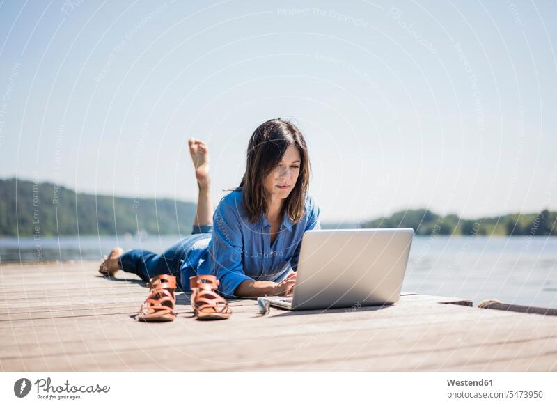 Mature woman working at a lake, using laptop on a jetty using a laptop Using Laptops At Work Laptop Computers laptops notebook lakes summer summer time summery