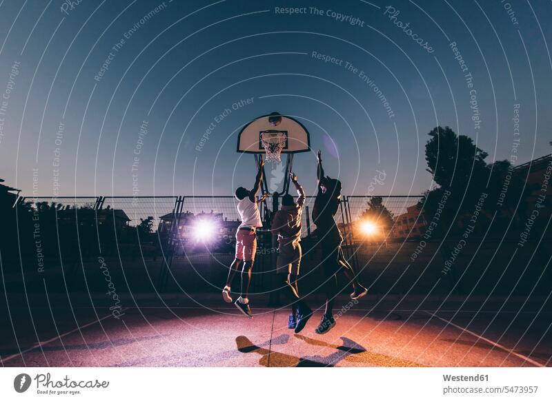 Male African friends playing basketball in court against clear sky at night color image colour image Spain leisure activity leisure activities free time