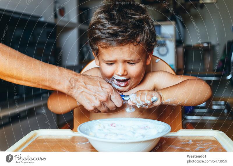 Little boy eating yogurt at home, hand of woman on the spoon Bowls dish dishes Plates Spoons help learn defiance supporting Emotions Feeling Feelings Sentiment
