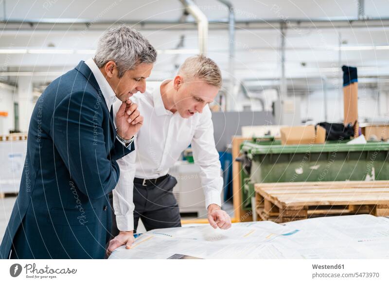 Two businessmen discussing paper in a factory business life business world business person businesspeople associate associates business associate