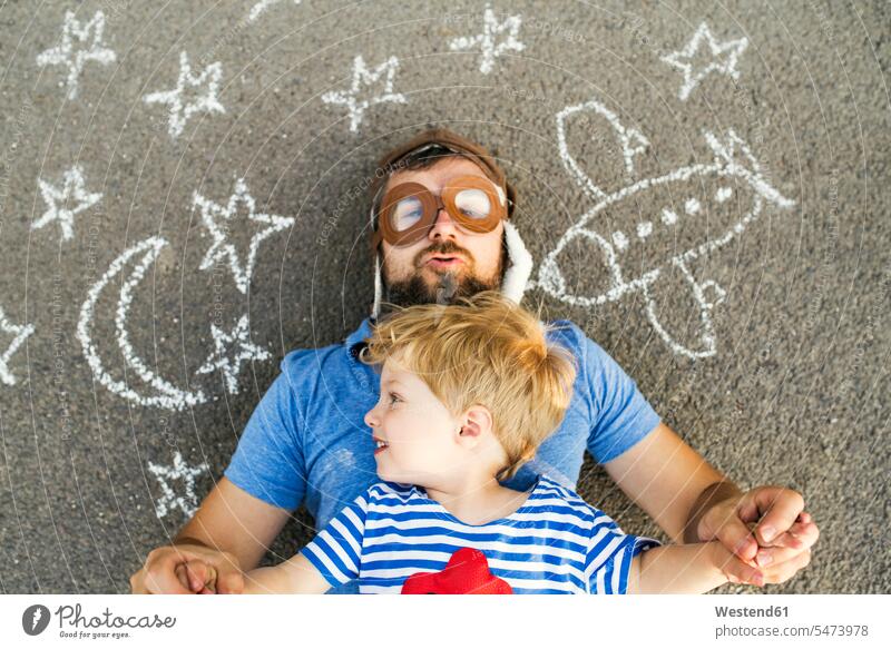 Portrait of mature man wearing pilot hat and his little son lying on asphalt painted with airplane, moon and stars Star Shape Star Shapes Star Shaped