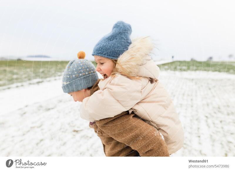 Boy carrying happy sister piggyback in winter landscape brother brothers sisters piggy-back pickaback Piggybacking Piggy Back hibernal happiness