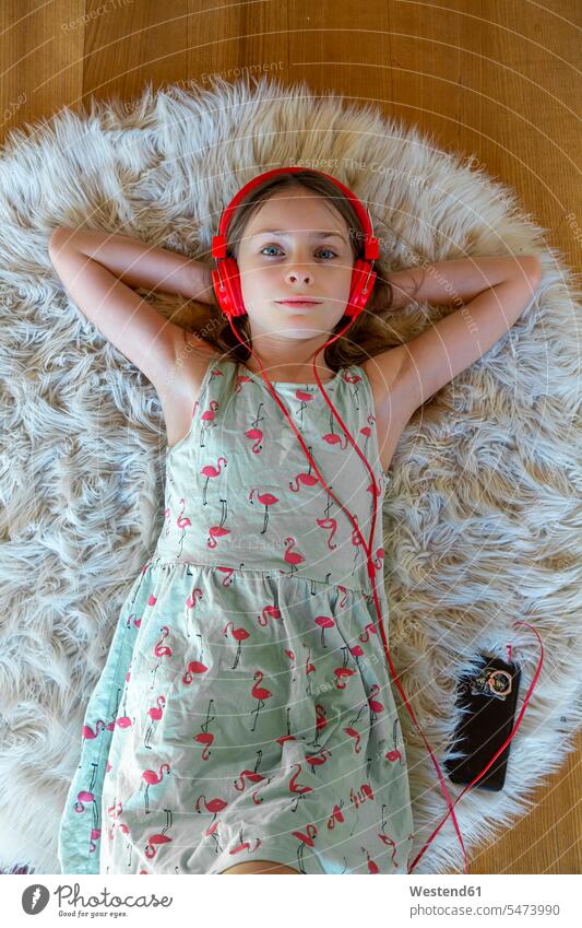 Girl lying on carpet at home listening to music with headphones and smartphone Germany hands behind head hands behind neck Hand Behind Head resting recreation