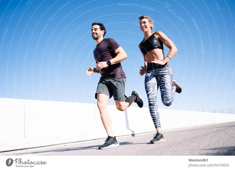 Smiling couple running on street against clear blue sky in city during summer color image colour image Spain outdoors location shots outdoor shot outdoor shots