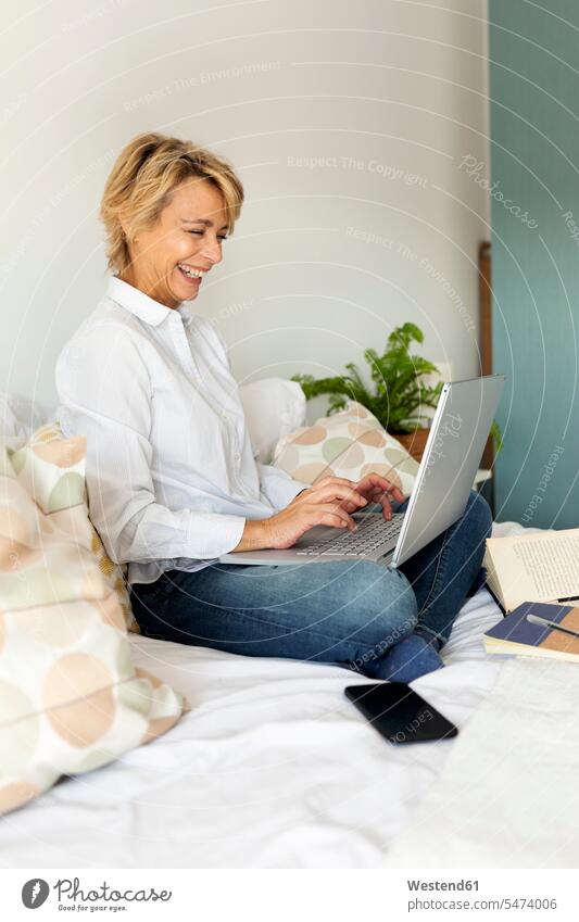 Happy mature woman sitting on bed at home using laptop human human being human beings humans person persons celibate celibates singles solitary people