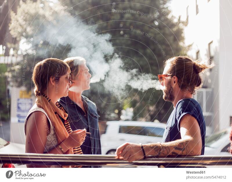 Friends smoking while standing outdoors on sunny day color image colour image location shots outdoor shot outdoor shots daylight shot daylight shots day shots
