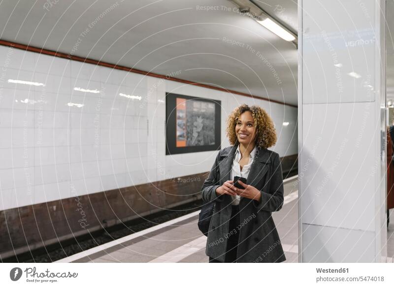Smiling woman with cell phone waiting in subway station business life business world business person businesspeople business woman business women businesswomen