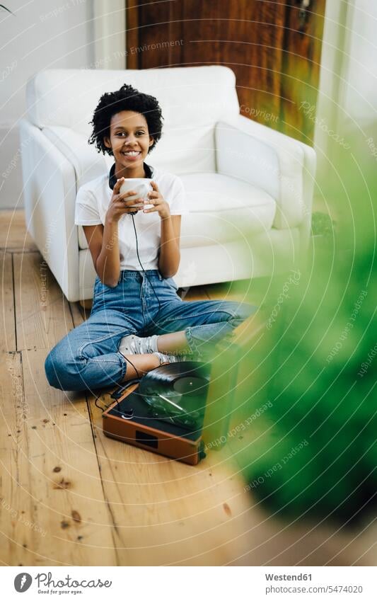 Young woman sitting on grounf listening music from record player, drinking coffee Coffee sitting on ground Sitting On The Floor Sitting On Floor headphones