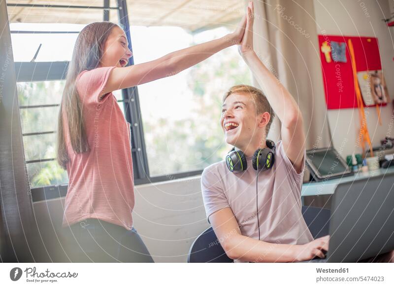 Happy teenage girl and boy with laptop high fiving Laptop Computers laptops notebook Teenage Girls female teenagers happiness happy boys males High Five Hi-Five