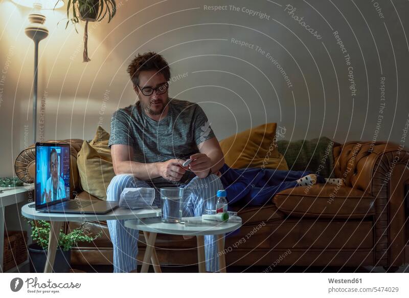 Man discussing over thermometer with doctor over video call while sitting by daughter at home color image colour image Home Interior Home Interiors