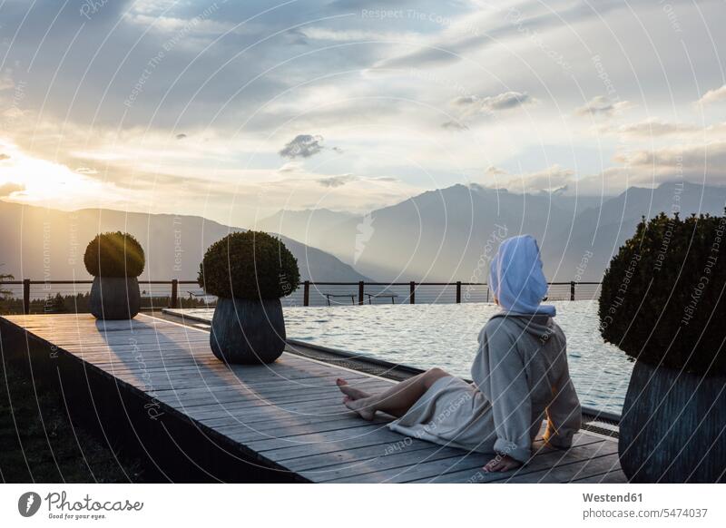 Woman relaxing at the poolside, wearing bathrobe and turban swimming pool swimming pools young women young woman Turbans sitting Seated relaxation bath robes