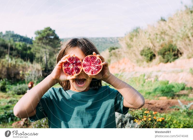 Boy standing in the countryside, covering eyes with halved pomegranates funny garden gardens eyes obscured Eyes covered Eye covered Hand Covering Eyes