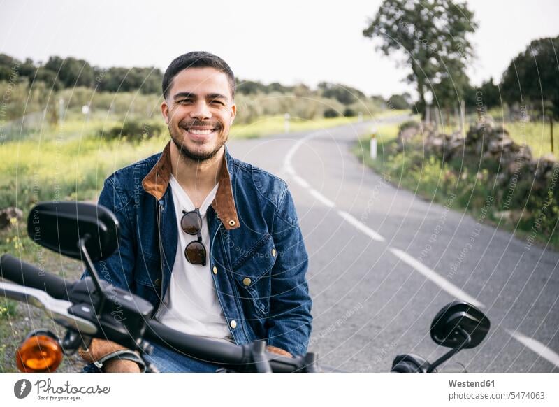 Smiling young biker sitting on motorcycle in countryside color image colour image Spain leisure activity leisure activities free time leisure time