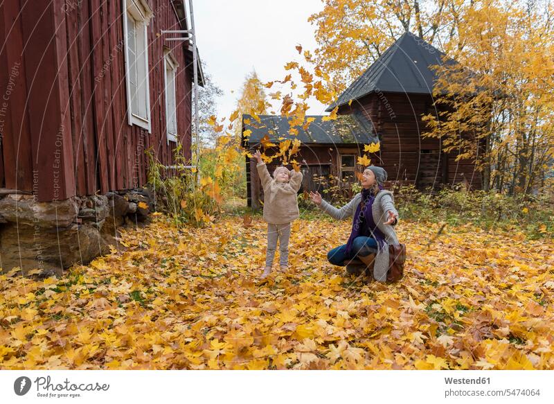 Finland, Kuopio, mother and little daughter throwing autumn leaves in the air mommy mothers ma mummy mama daughters parents family families people persons