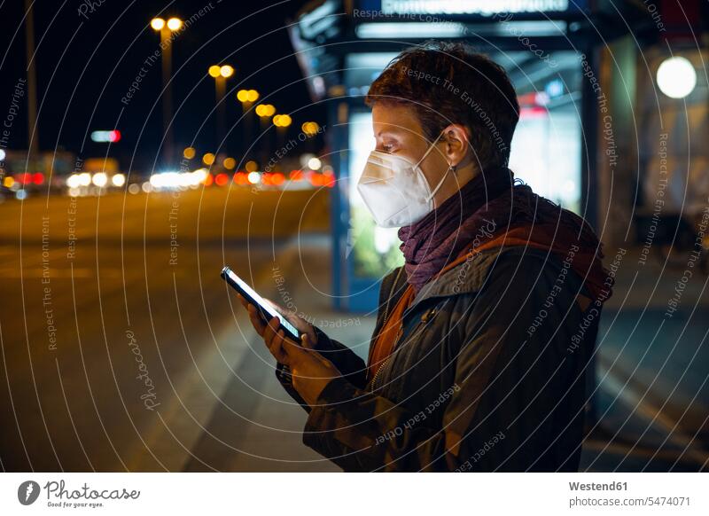 Woman wearing FFP2 mask using smart phone while waiting for bus in city color image colour image outdoors location shots outdoor shot outdoor shots Germany