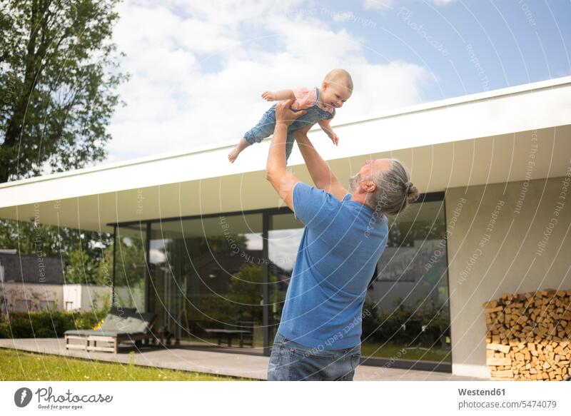 Happy mature man lifting up baby girl in garden of his house human human being human beings humans person persons caucasian appearance caucasian ethnicity